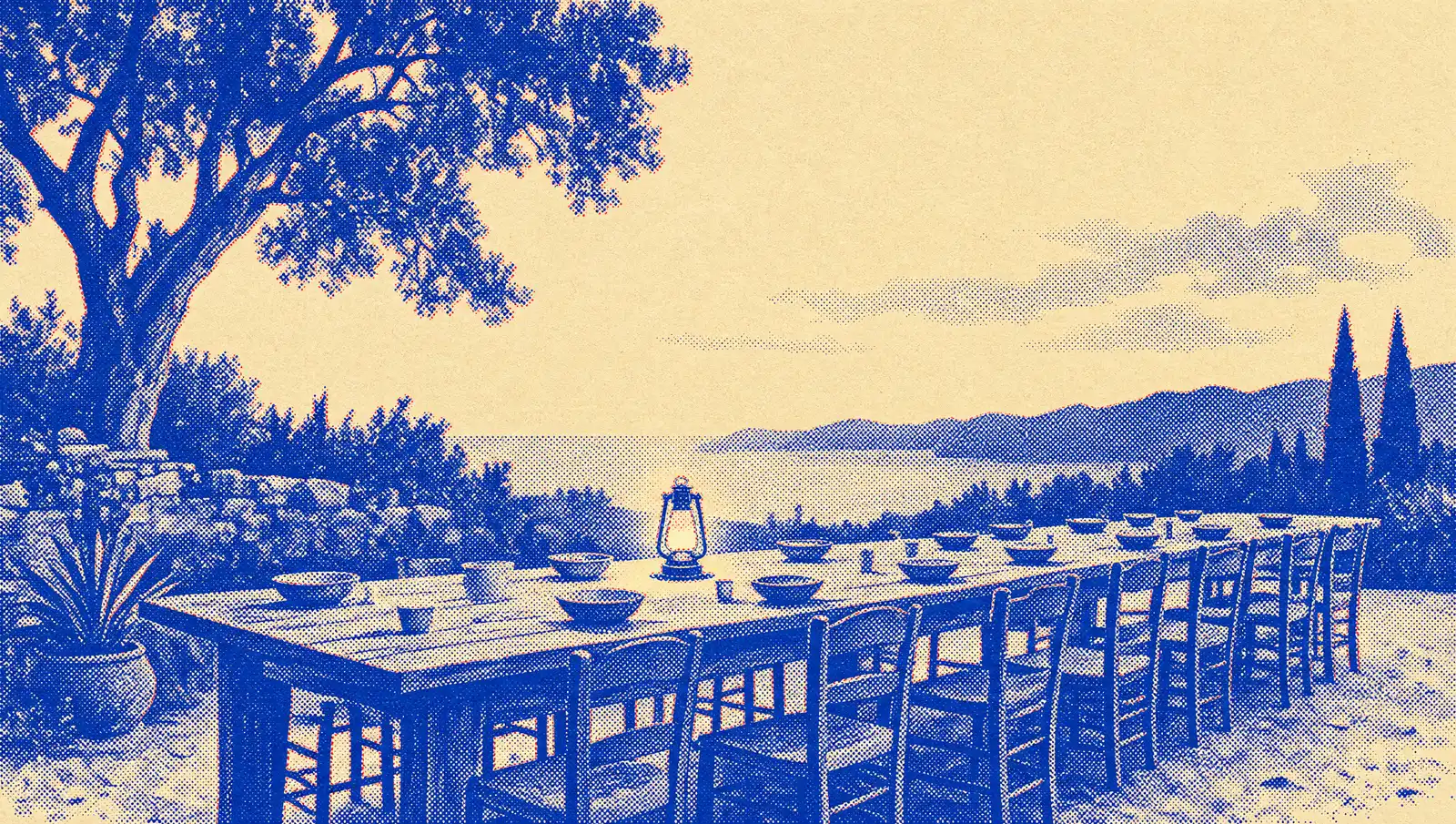 A long outdoor table set with bowls and empty chairs at dusk, a small lantern glowing at its center